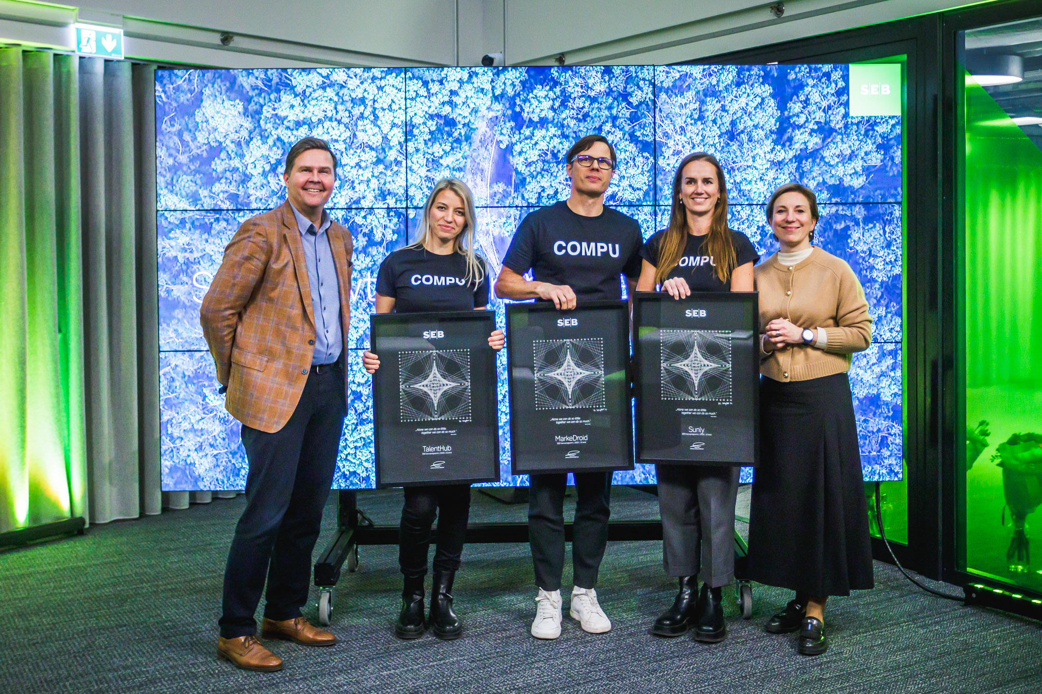SEB growth-program participants holding their framed awards in front of a video wall